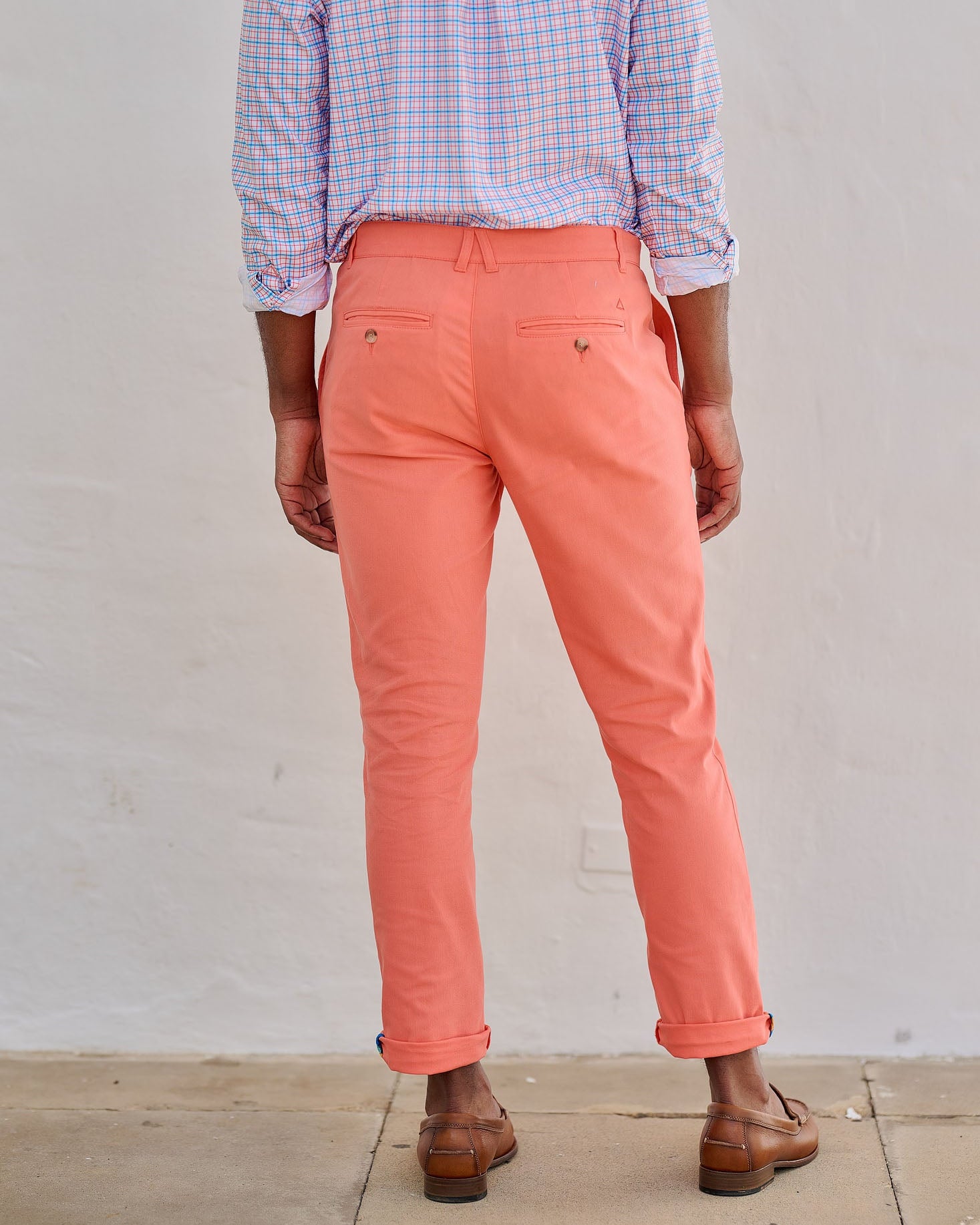 Person wearing coral pants and a checkered shirt against a plain background