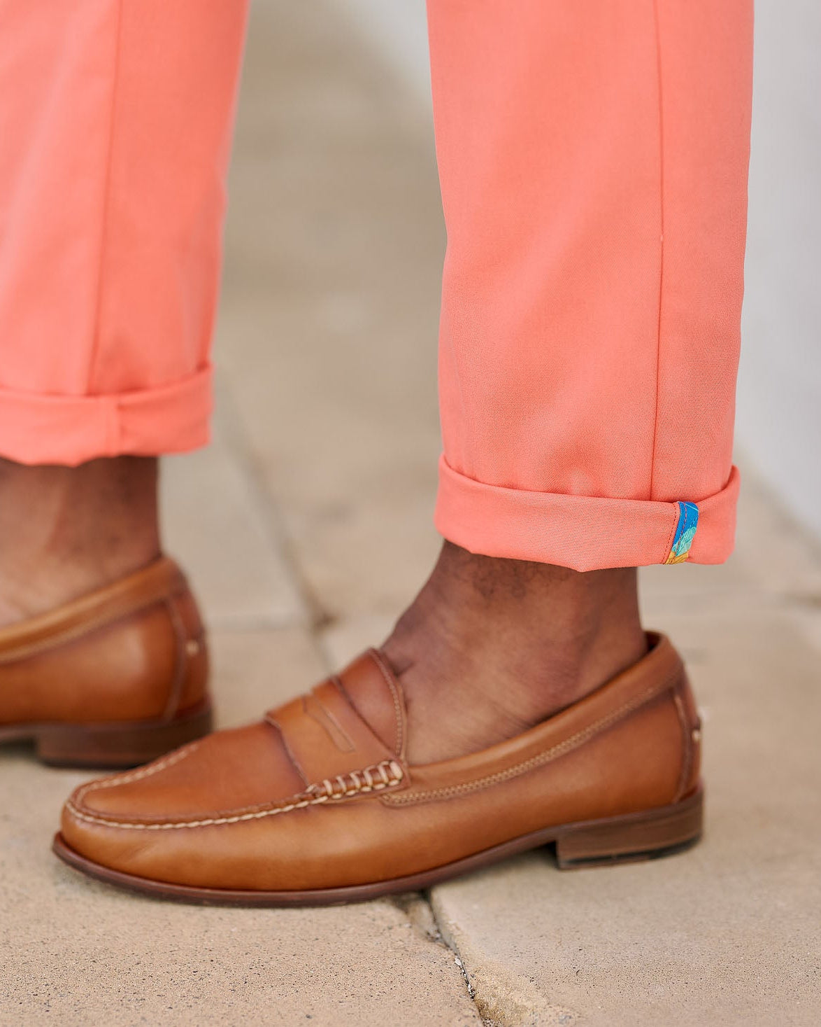 Brown loafers worn with coral pants on a neutral background