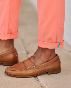 Brown loafers worn with coral pants on a neutral background