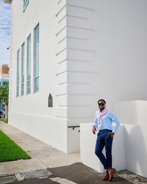 Man leaning against a white building wall wearing sunglasses and a light blue shirt.
