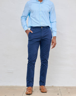 Man wearing a light blue checkered shirt and dark blue pants against a plain background