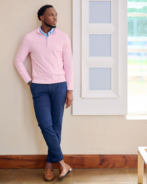 Man wearing a pink sweater and blue pants standing indoors.