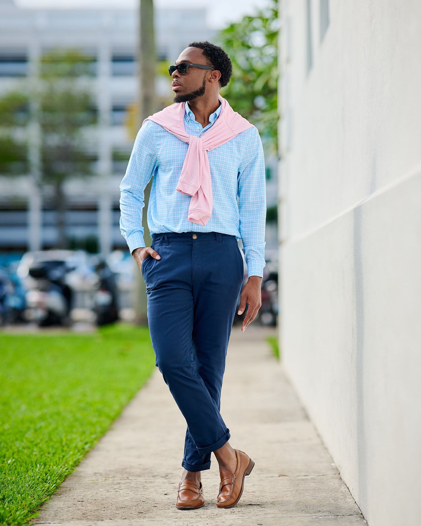 Man walking outdoors wearing a light blue shirt, navy pants, and a pink scarf.