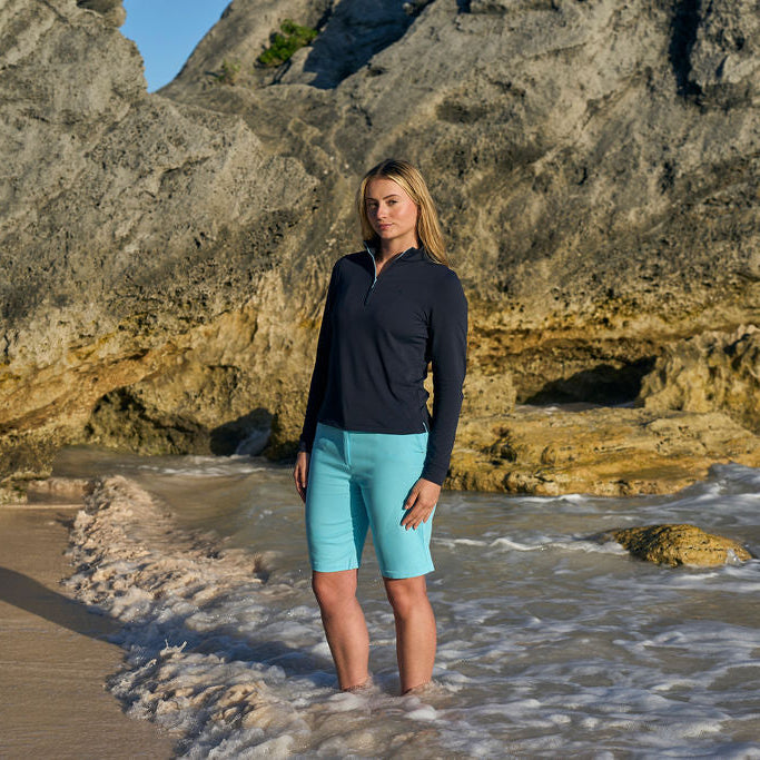 Person standing on a rocky beach wearing a black long-sleeve shirt and light blue shorts.