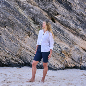 Woman standing on a sandy beach with a rocky cliff in the background