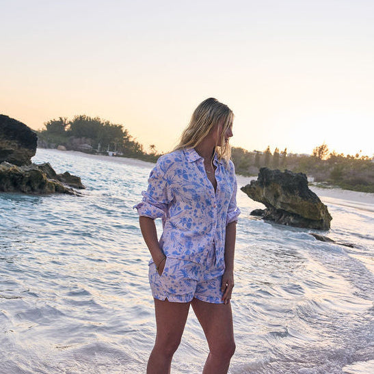 Woman standing on a beach at sunset with rocks and water in the background